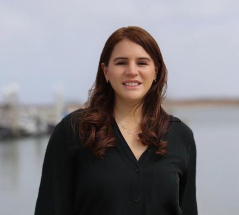 Mariana Rivera-Higueras 3 Mariana Rivera-Higueras wears a black long-sleeved blouse and stands smiling in front of an ocean shoreline.
