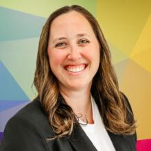 Amanda Boardman A woman wears a black blazer and smiles in front of a colorful background.