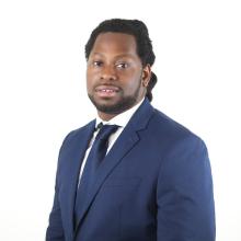 A man in a blue suit stands in front of a white background