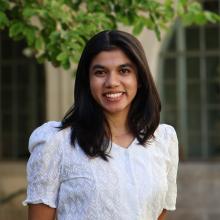 A person in a white shirt stands outdoors in front of a building.