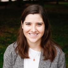 A person in a grey blazer stands outdoors.