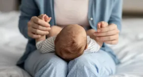 A baby lays in a woman's lap on a bed. The woman wears a blue cardigan and blue pants with white polka dots.