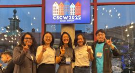 Five students make the Hook-em sign in front of a glass window.