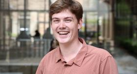A man wears a polo shirt and stands in an outdoor space.