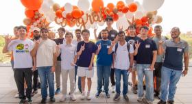 A group of students make the Hook 'em sign in front of orange and white balloons, one of which spells "congrats."