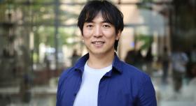 A man wears a blue jacket and stands outdoors.