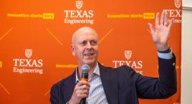 A person in a business suit speaks into a microphone in front of a Texas Engineering banner.