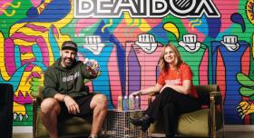 Two people sit in front of a colorful mural advertising Beatbox drinks.