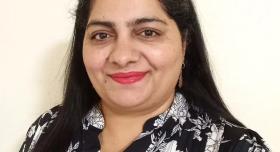 A person wears a black and white floral shirt and stands in front of a white background.