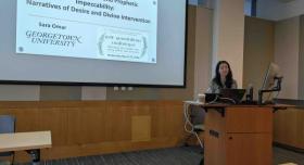 A person stands at a podium and gives a presentation in a conference room.