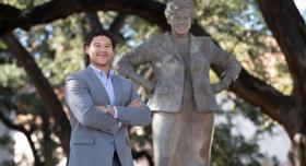 A person in a suit stands with their arms crossed next to a statue of Barbara Jordan.