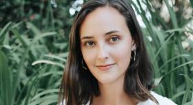 A person poses for a headshot in front of blades of tall grass.