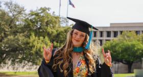 A person in graduation regalia poses in front of the LBJ library.