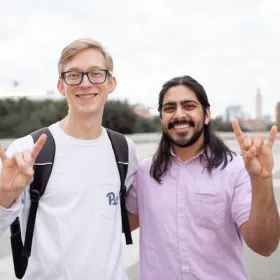 two students outside using hook 'em horns gesture