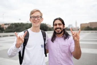 two students outside using hook 'em horns gesture