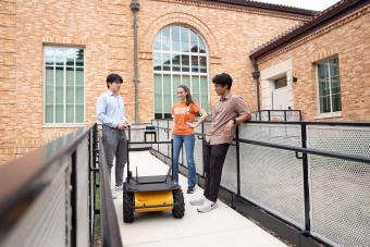 three students outside with robot