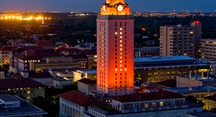 The UT Tower is illuminated in red light, standing tall over Austin, Texas, in early evening.