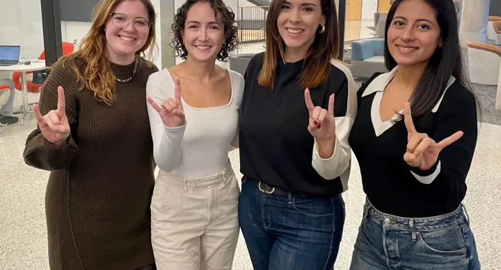 MBA students Michelle Jennings, from left, Cecilia Gonzalez, Ana Keren Carretero, and Alondra Villarreal make "hook 'em horns" signs inside an academic building.