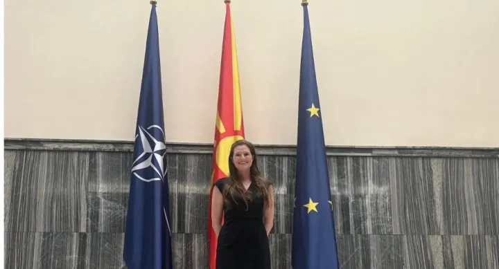 A woman in a black dress stands in front of three Macedonian flags inside a building in North Macedonia.