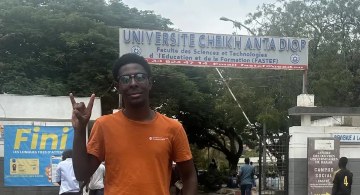 Devarier Smith wears an orange shirt and makes the hook 'em horns sign in front of the Universite Cheikh Anta Diop in Senegal.