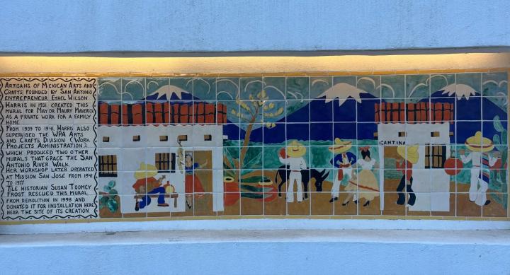 A mural of glazed tiles depicting a mountain village with white buildings and people dancing.