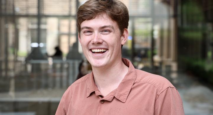 A man wears a polo shirt and stands in an outdoor space.