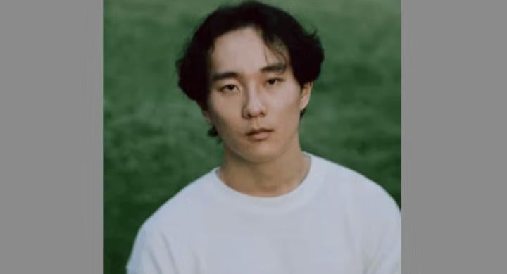 A man wears a white t-shirt against a green background.