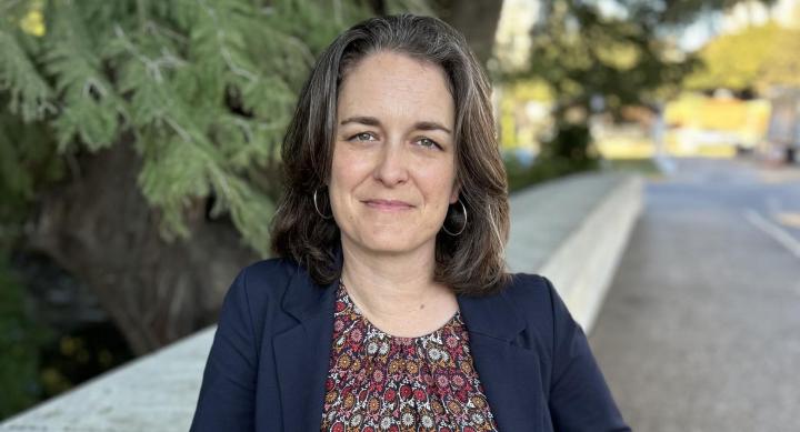 A woman wears businesswear and stands outdoors.