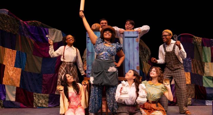 A theatre cast poses in full costume on a stage.