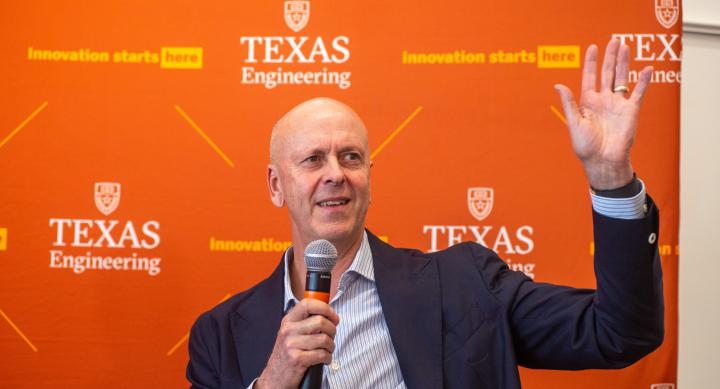 A person in a business suit speaks into a microphone in front of a Texas Engineering banner.