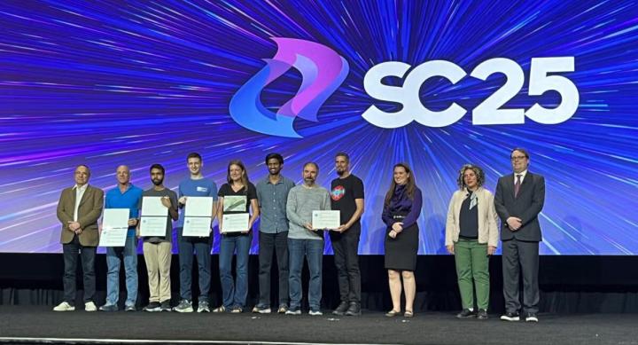 Eleven people stand onstage at SC25 holding certificates.