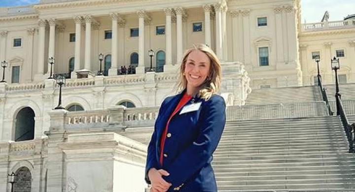 A person in businesswear stands in front of the Texas Capitol building.