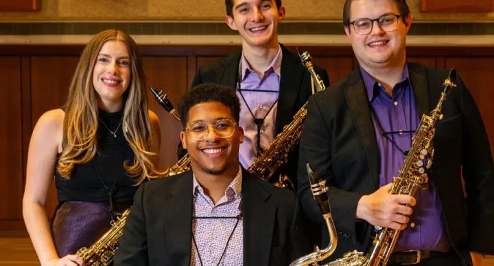 Four people pose for a group photo holding saxophones.