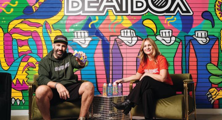 Two people sit in front of a colorful mural advertising Beatbox drinks.