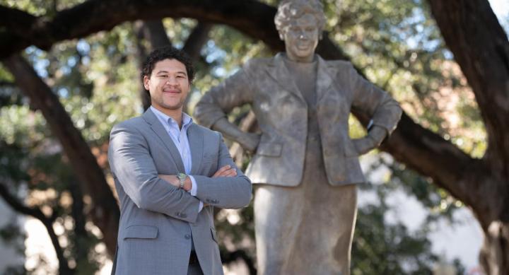 A person in a suit stands with their arms crossed next to a statue of Barbara Jordan.