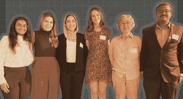 A group of students and their professor stand in front of a grey background.