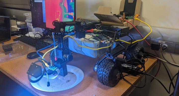 A robot on wheels sits on a table next to a computer.