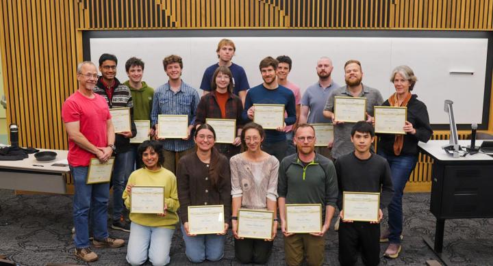 A group of students pose for a group photo holding their certificates in a classroom.