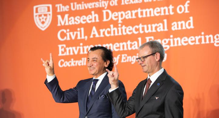 Two people in suits make the Hook 'em hand sign in front of a banner for the Maseeh Department.