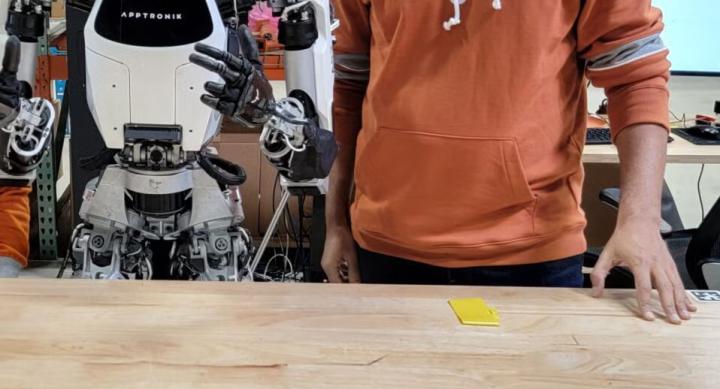 A person in a Longhorn sweater stands next to a robot.
