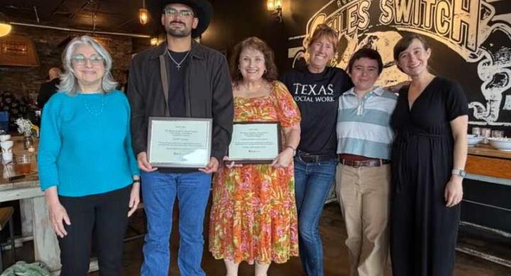 A group poses for a photo around two people holding certificates.