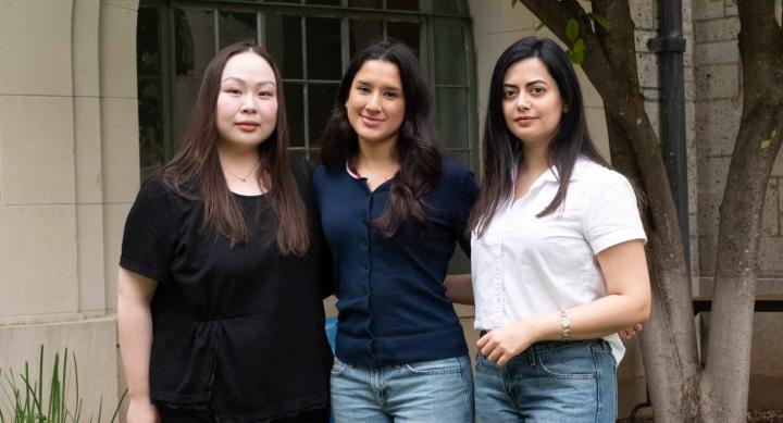 Three students pose for a group photo in front of a campus building.