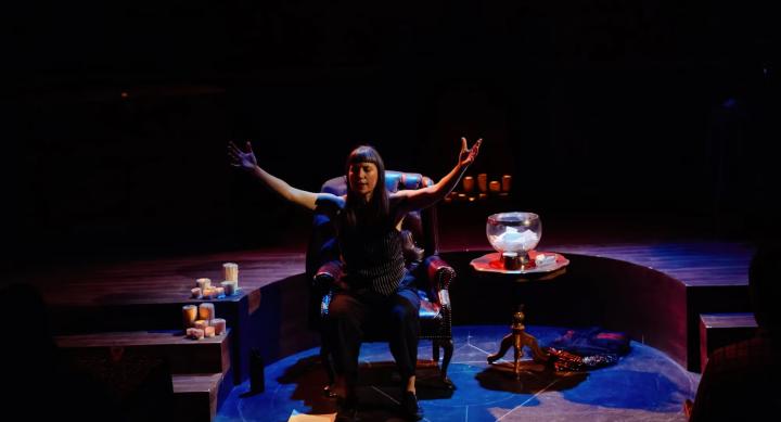 A person sits in armchair and performs on a stage.