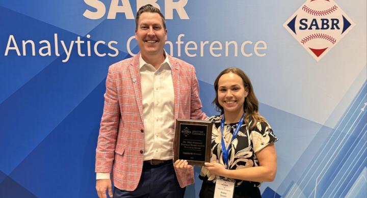 Two people pose with a certificate in front of a backdrop for the SABR Analytics Conference.