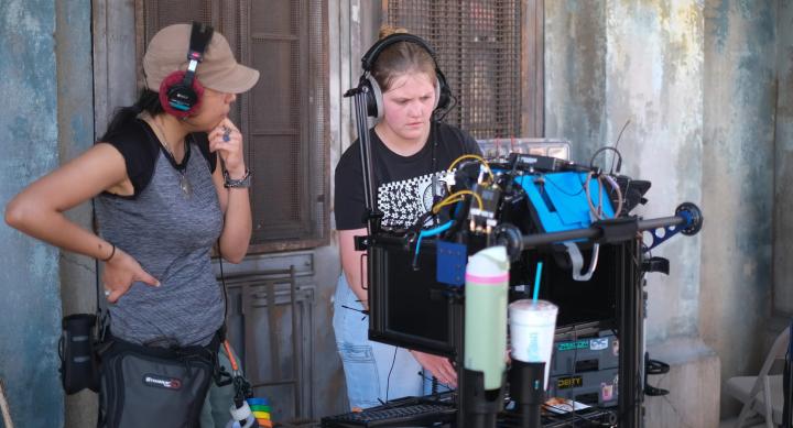 Two students operate equipment on a film set.