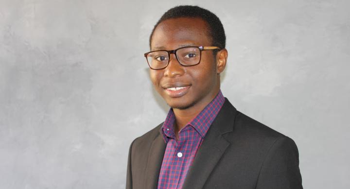 Ayobami Aiyeolemi wears a suit and poses in front of a grey background.