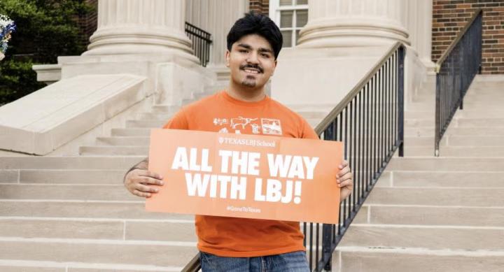 Caleb Garcia stands on some outdoor steps with an orange sign reading "All the Way with LBJ!"
